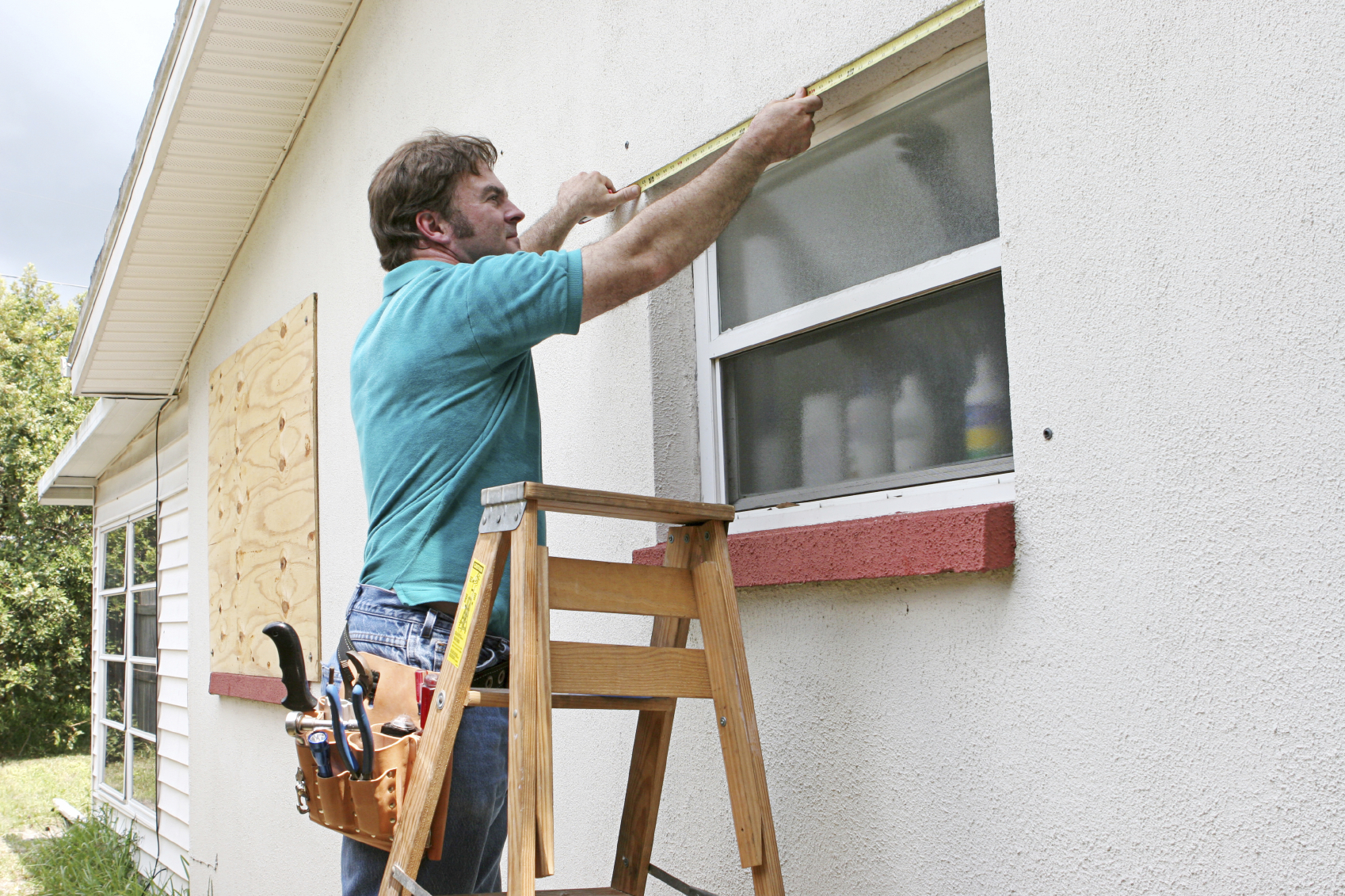 A man measuring windows for hurricane shutters or plywood.